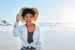 Woman in blue striped shirt and straw hat smiling at the beach
